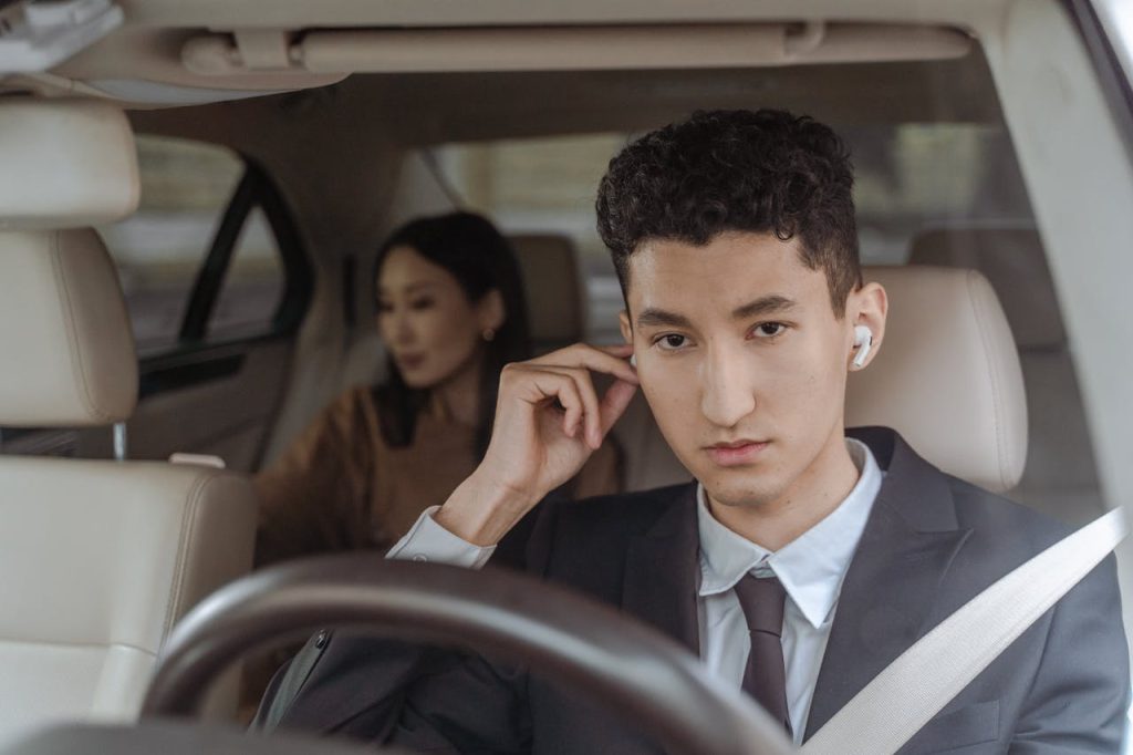 A professional driver in a suit with AirPods driving a female passenger in a car.